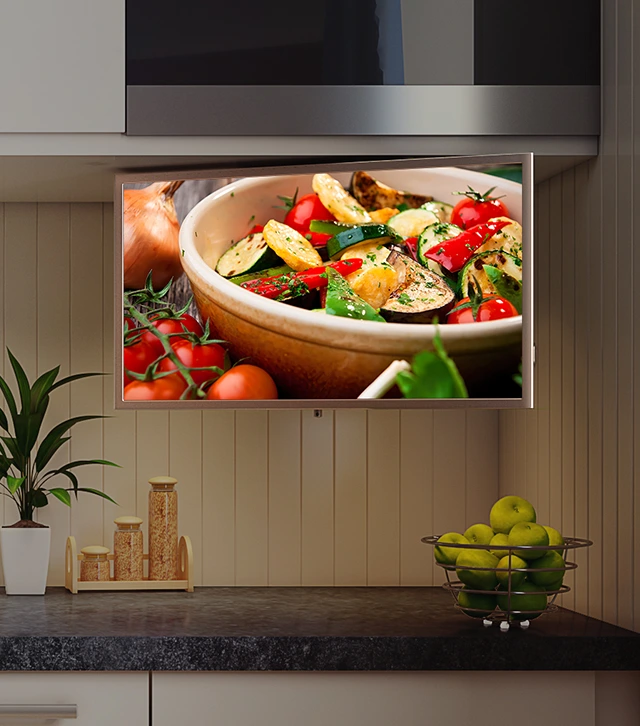  A slim, flat-panel kitchen smart tv custom-mounted beneath the upper kitchen cabinetry, directly above the countertop at eye-level when you’re standing at the counter.